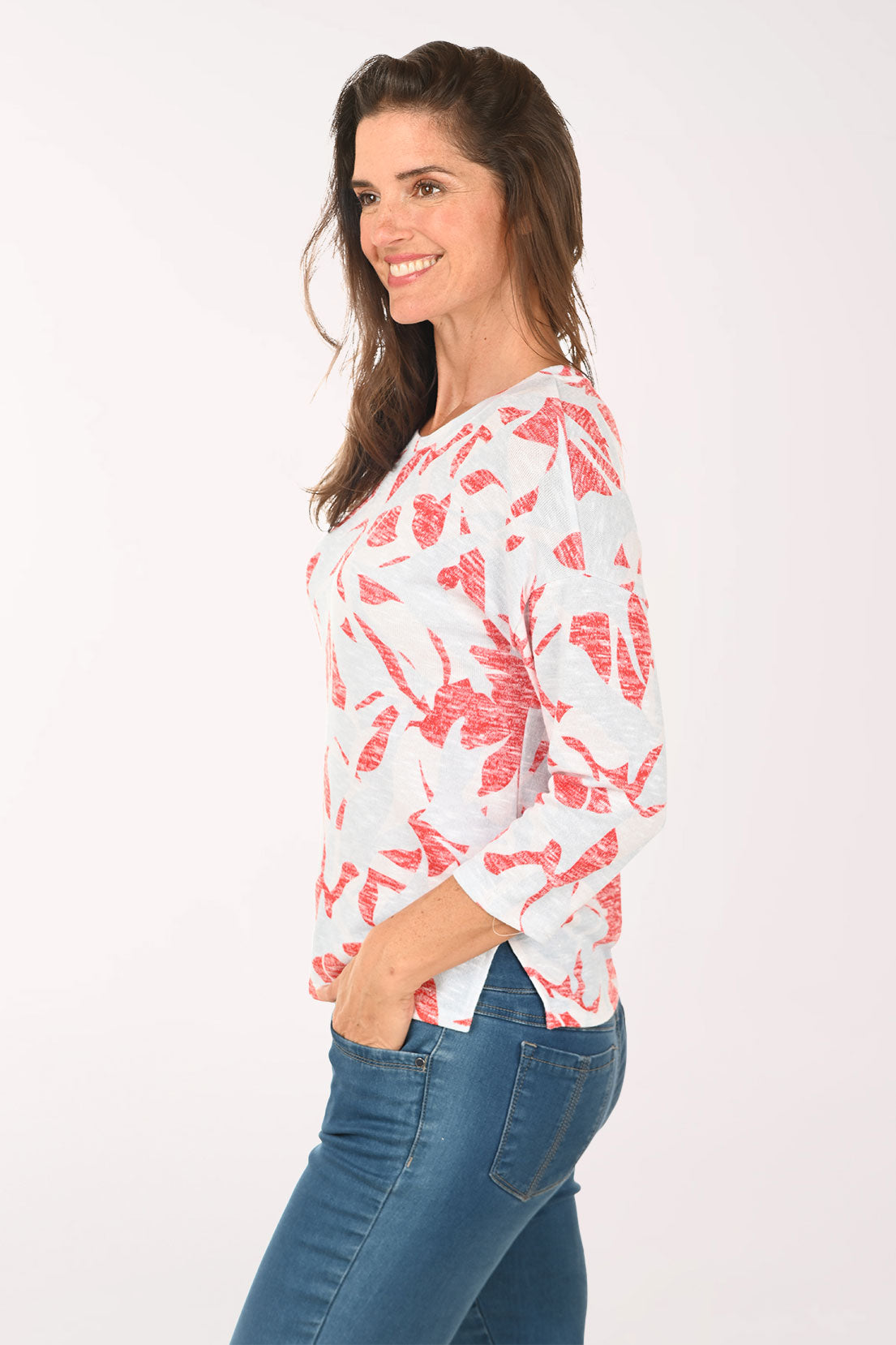 Woman wearing a white top with red floral pattern and blue jeans on a white background