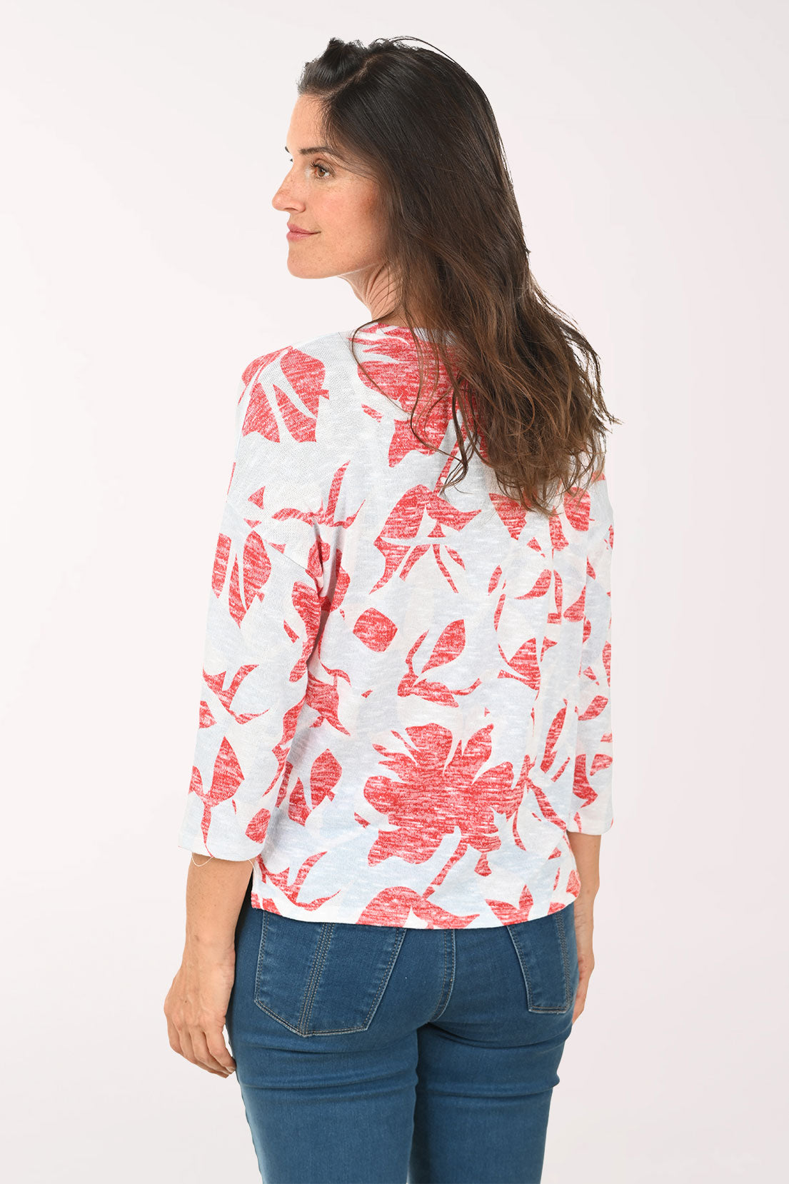 Woman wearing a white top with red floral pattern and blue jeans on a white background