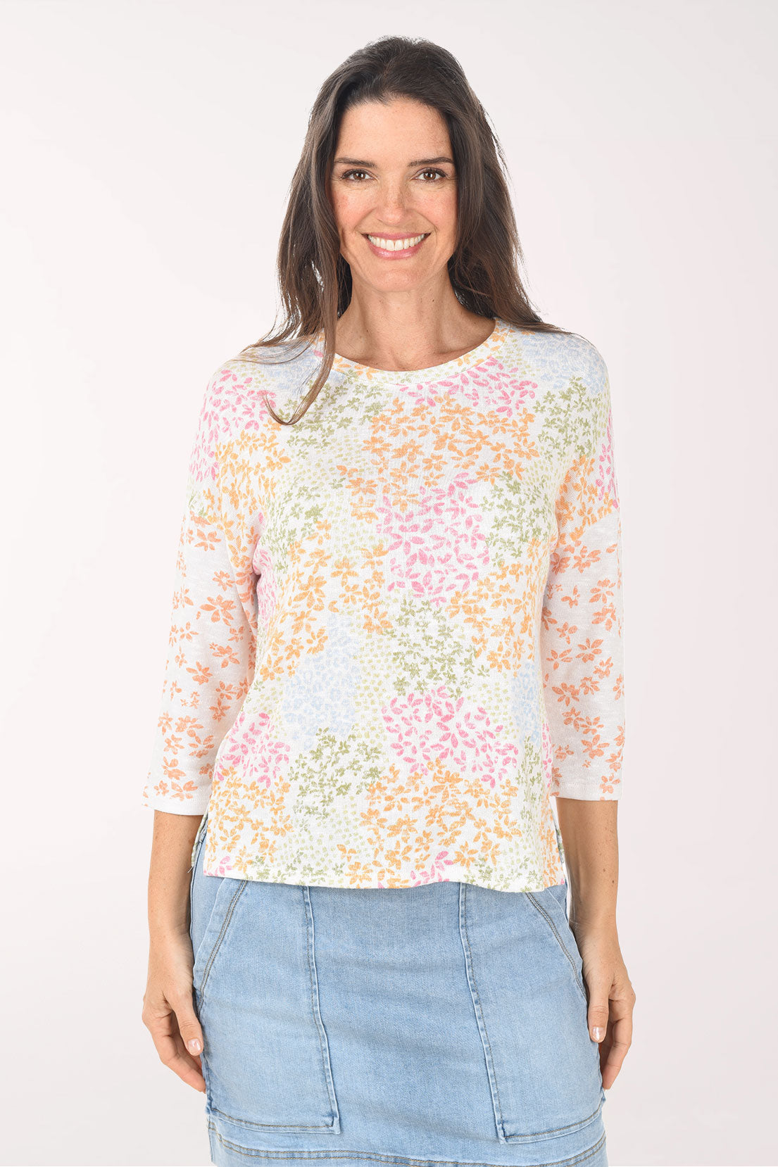 Woman wearing a pastel floral top and denim skirt on a white background
