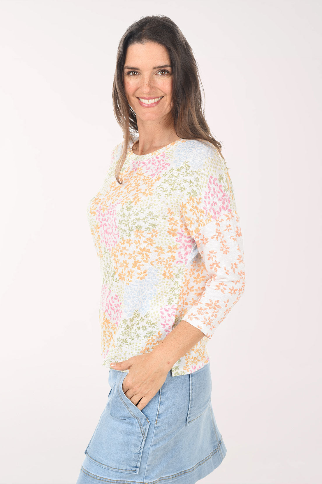 Woman wearing a pastel floral top and denim skirt on a white background