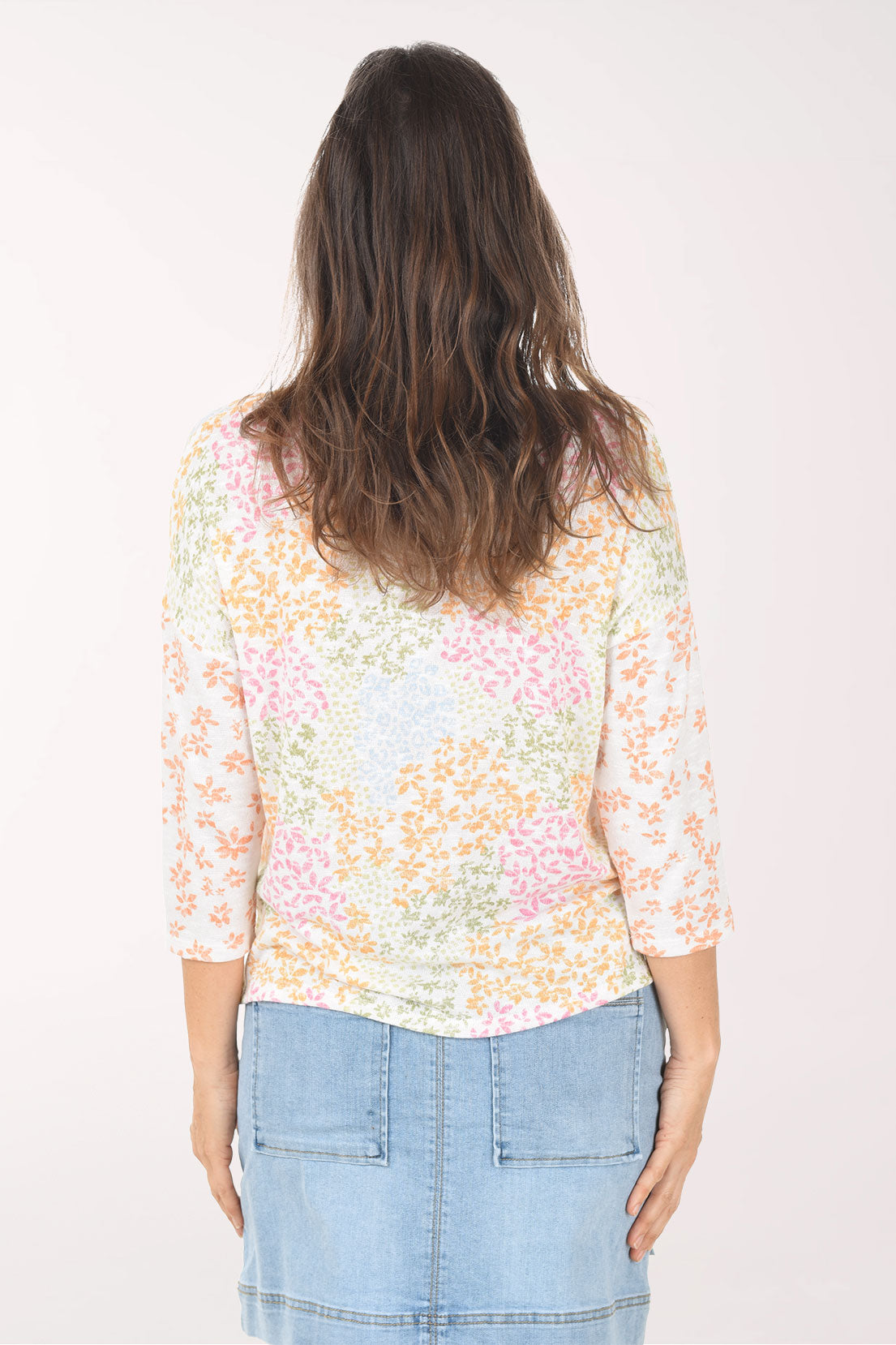 Woman wearing a pastel floral top and denim skirt on a white background