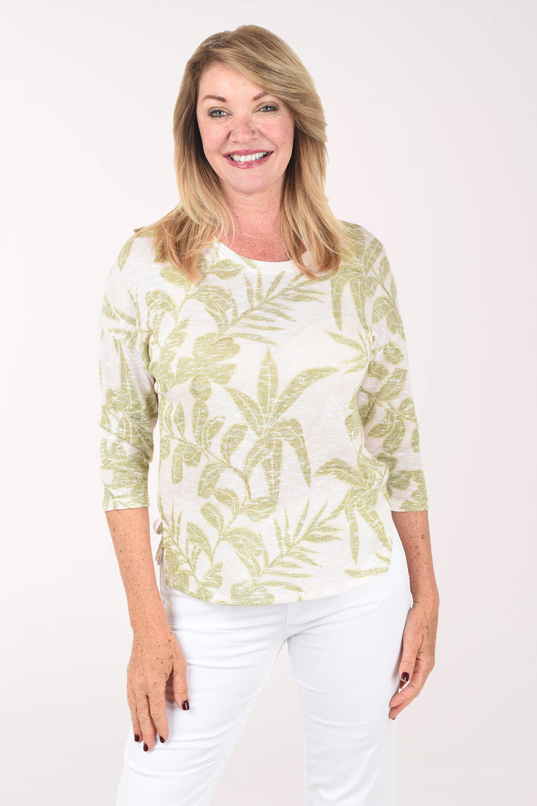 Woman wearing a light green and white patterned top with white pants on a white background