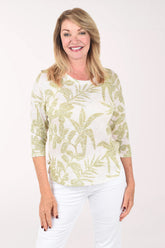 Woman wearing a light green and white patterned top with white pants on a white background