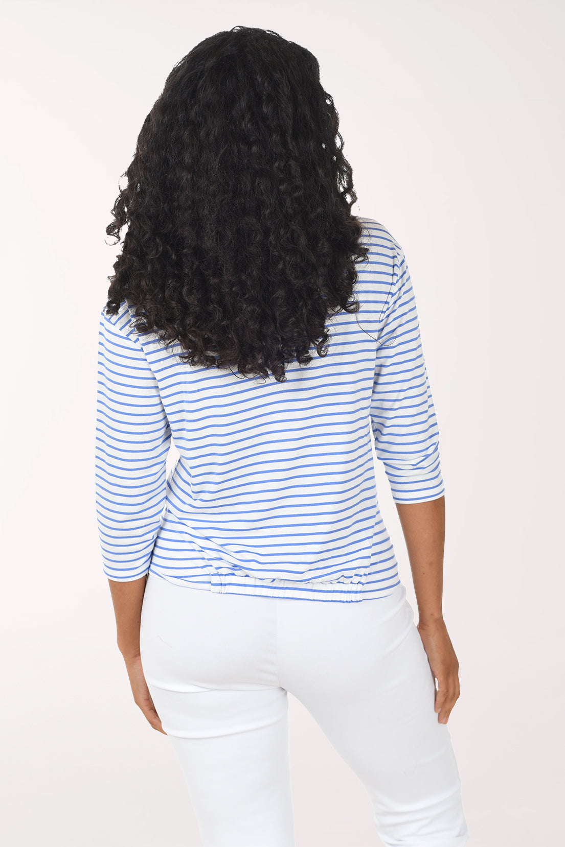 Woman wearing a blue and white striped shirt and white pants on a white background