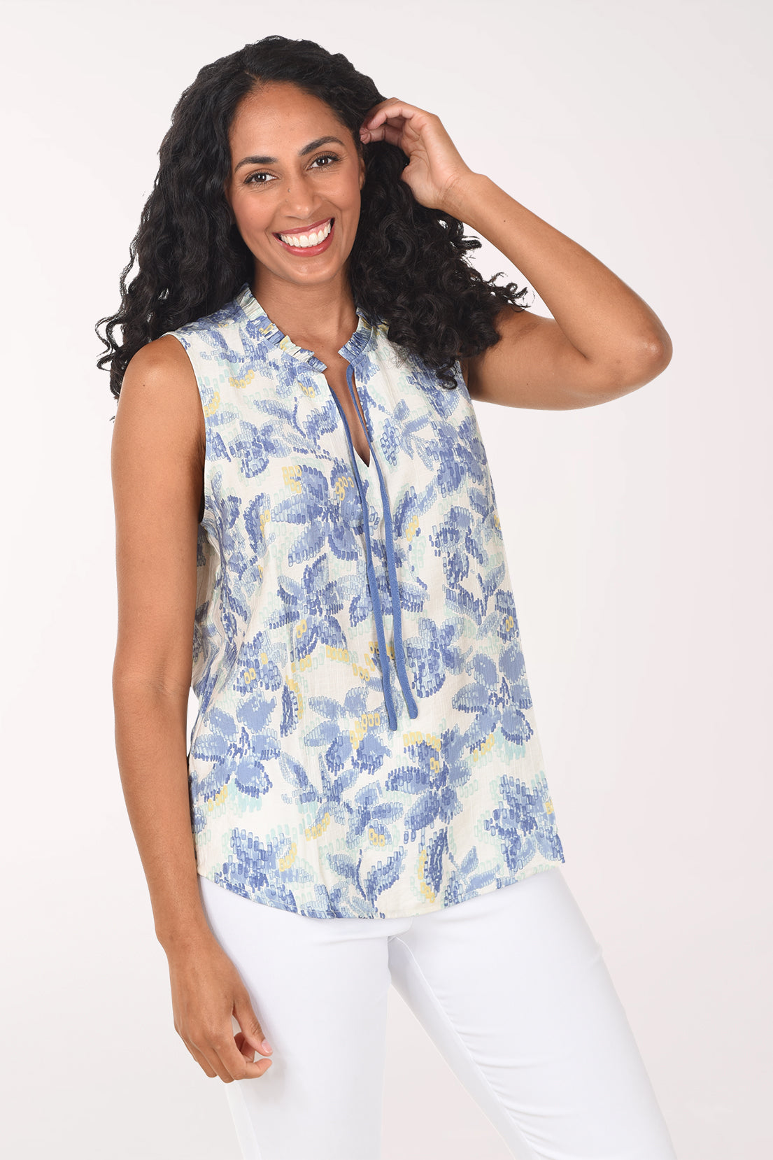 Woman wearing a sleeveless floral top and white pants on a white background