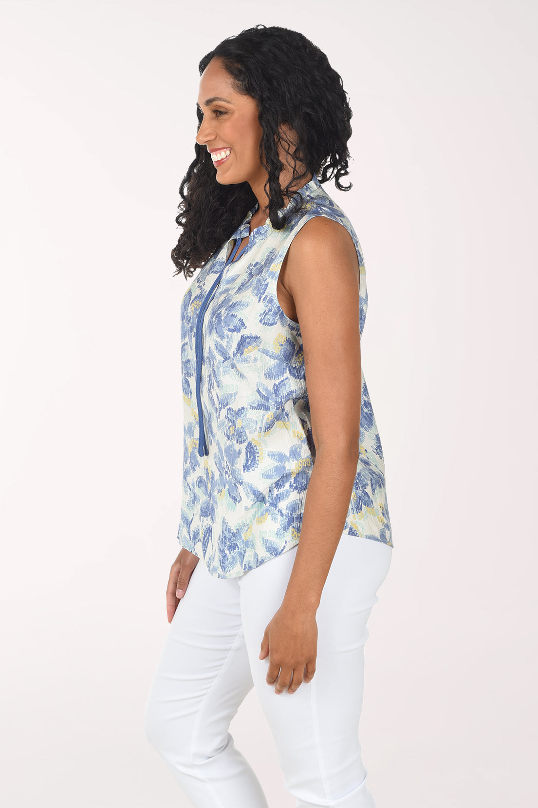 Woman wearing a sleeveless floral top and white pants on a white background