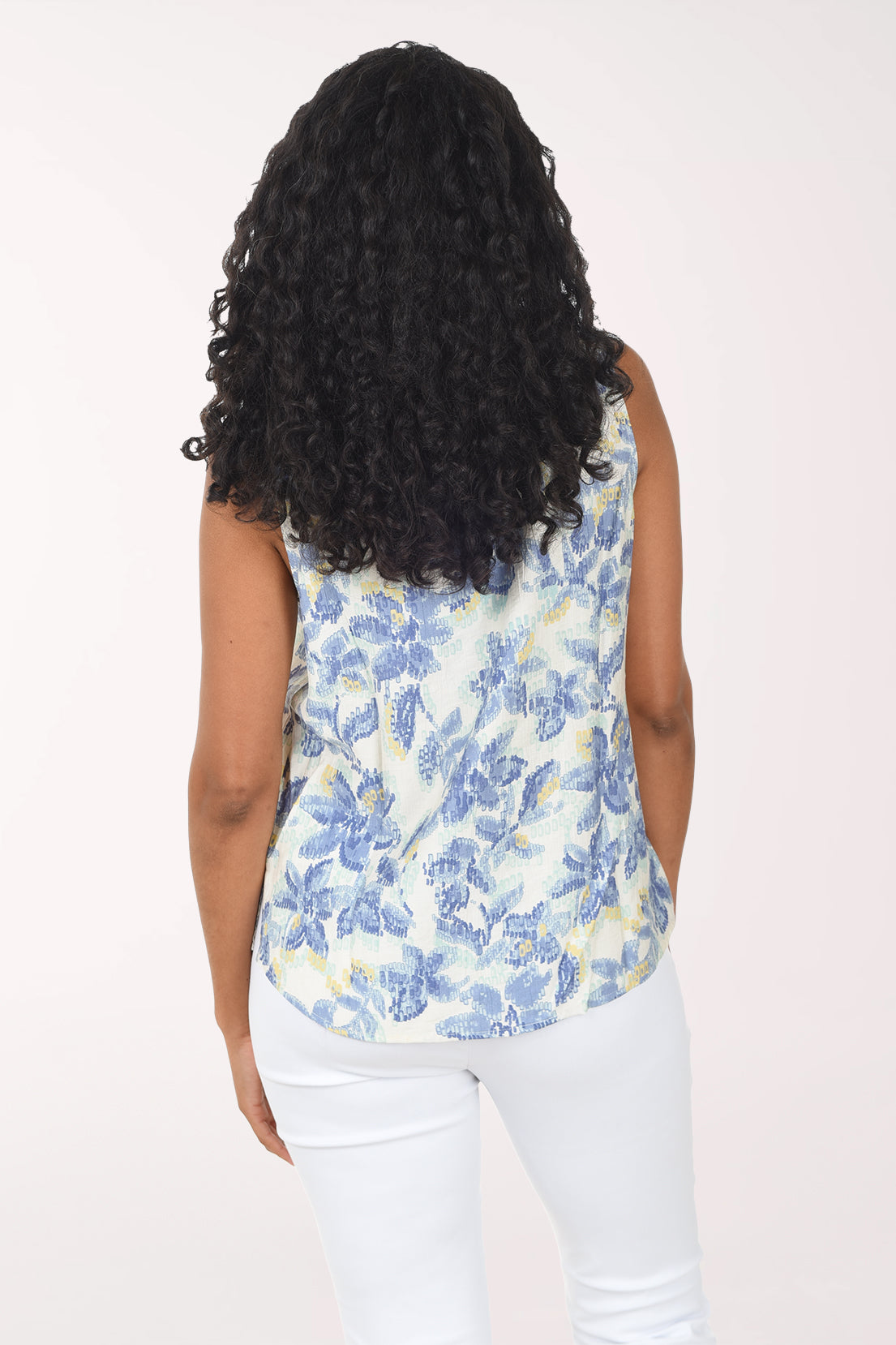 Woman wearing a sleeveless floral top and white pants on a white background