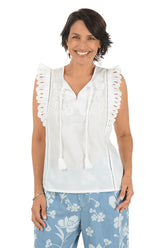 Woman wearing a white sleeveless top with lace details and blue floral pants on a white background