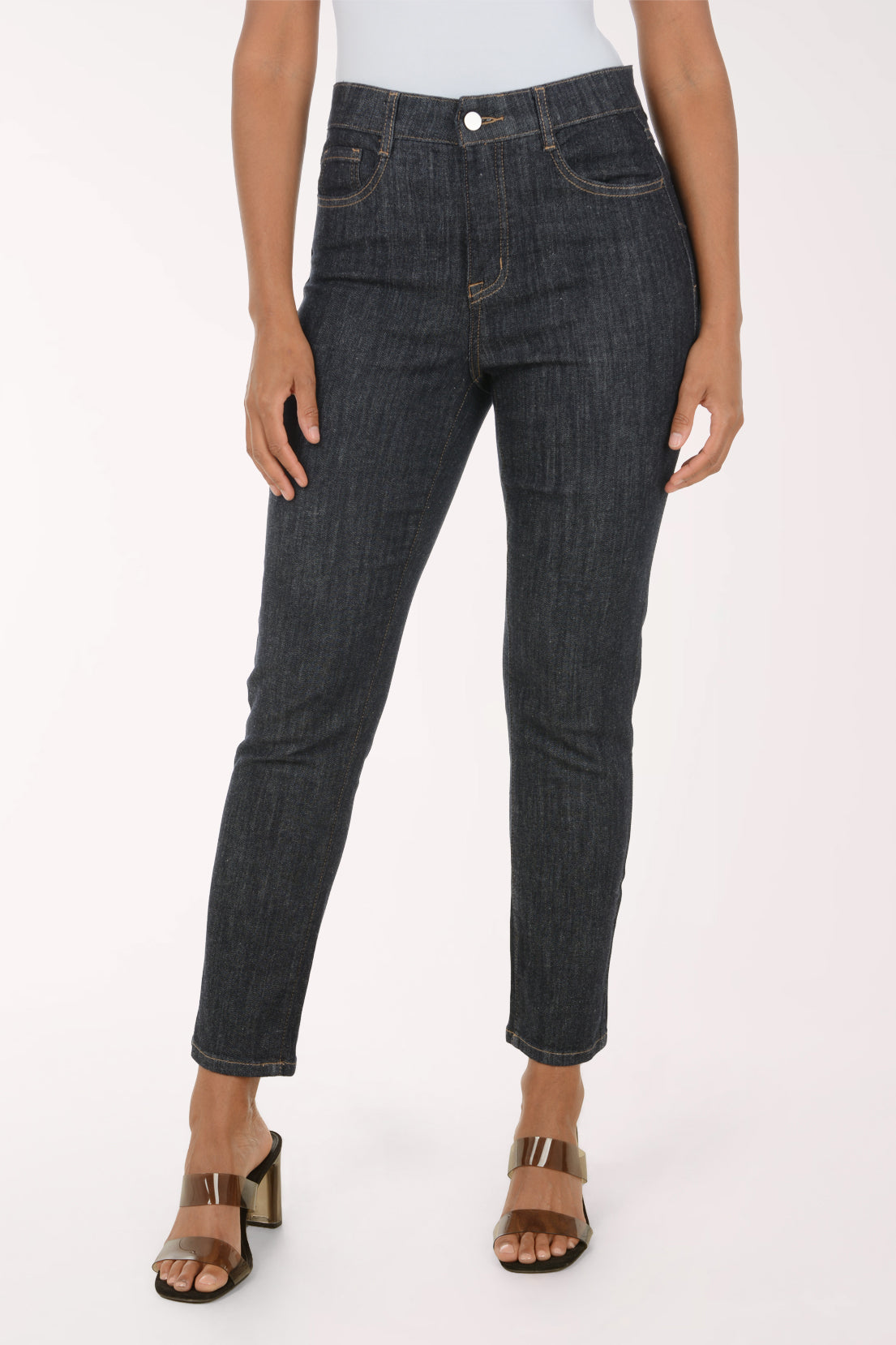 A model wearing dark gray slim-fit denim jeans with a light gray top and metallic brown heeled sandals, shown from the waist down against a plain white studio background.