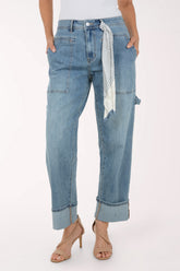 A model wearing light-wash blue denim jeans with a rolled cuff, side cargo pockets, and a striped fabric tie belt, paired with beige high-heeled sandals against a plain white background.