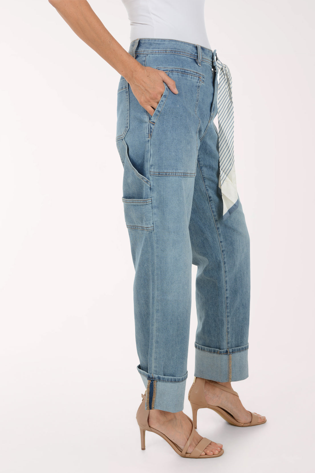 A model wearing light-wash blue denim jeans with a rolled cuff, side cargo pockets, and a striped fabric tie belt, paired with beige high-heeled sandals against a plain white background.