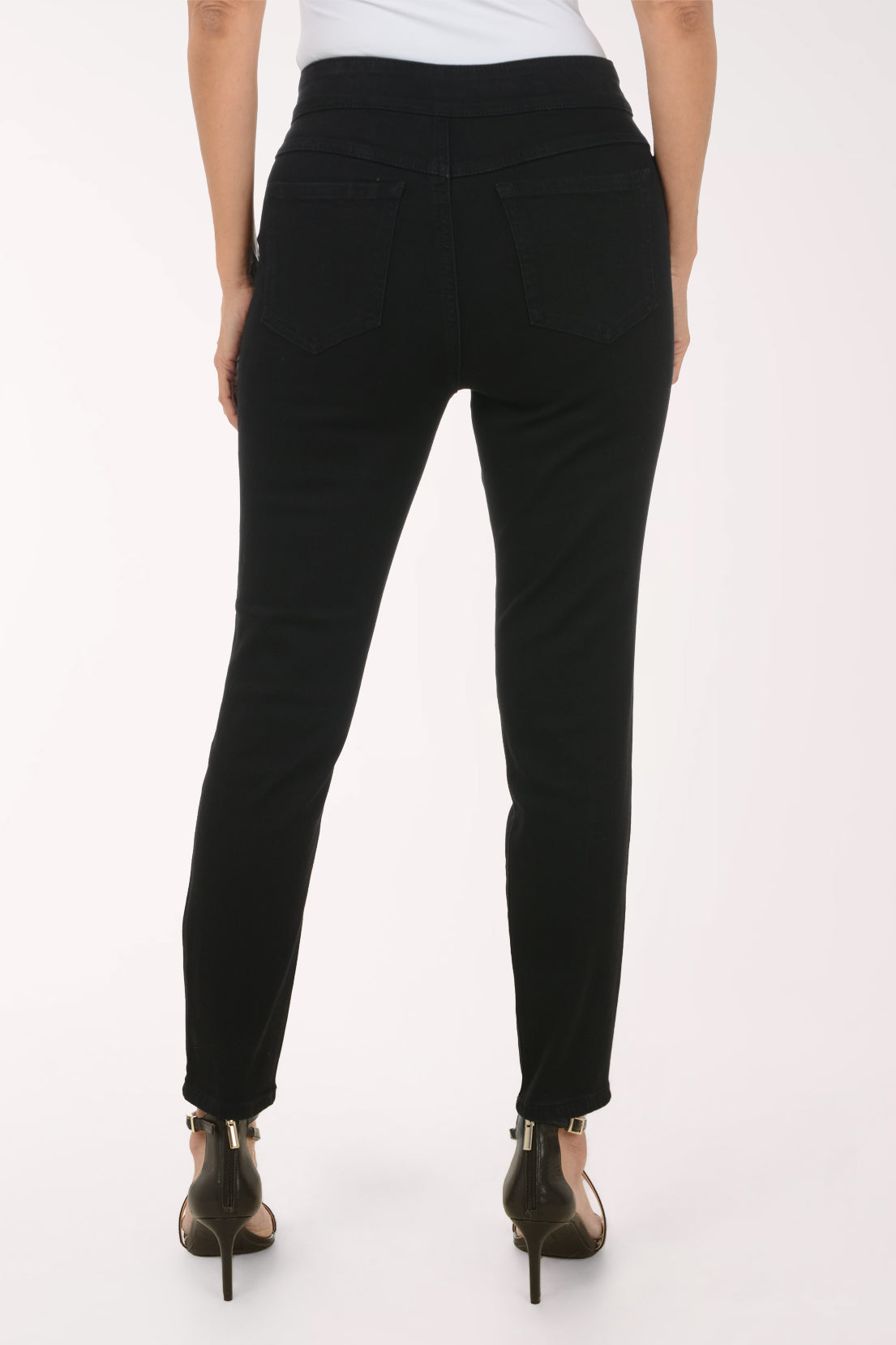 A model wearing black slim-fit ankle-length jeans with a high waist, paired with a white top and black strappy heels, shown against a plain white studio background.