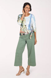 Full-length front view of a woman in sage green Moss stretch denim wide leg crop pants with a high-rise waist, worn with a multicolor abstract print three-quarter sleeve top tied at the waist and nude strappy heels.