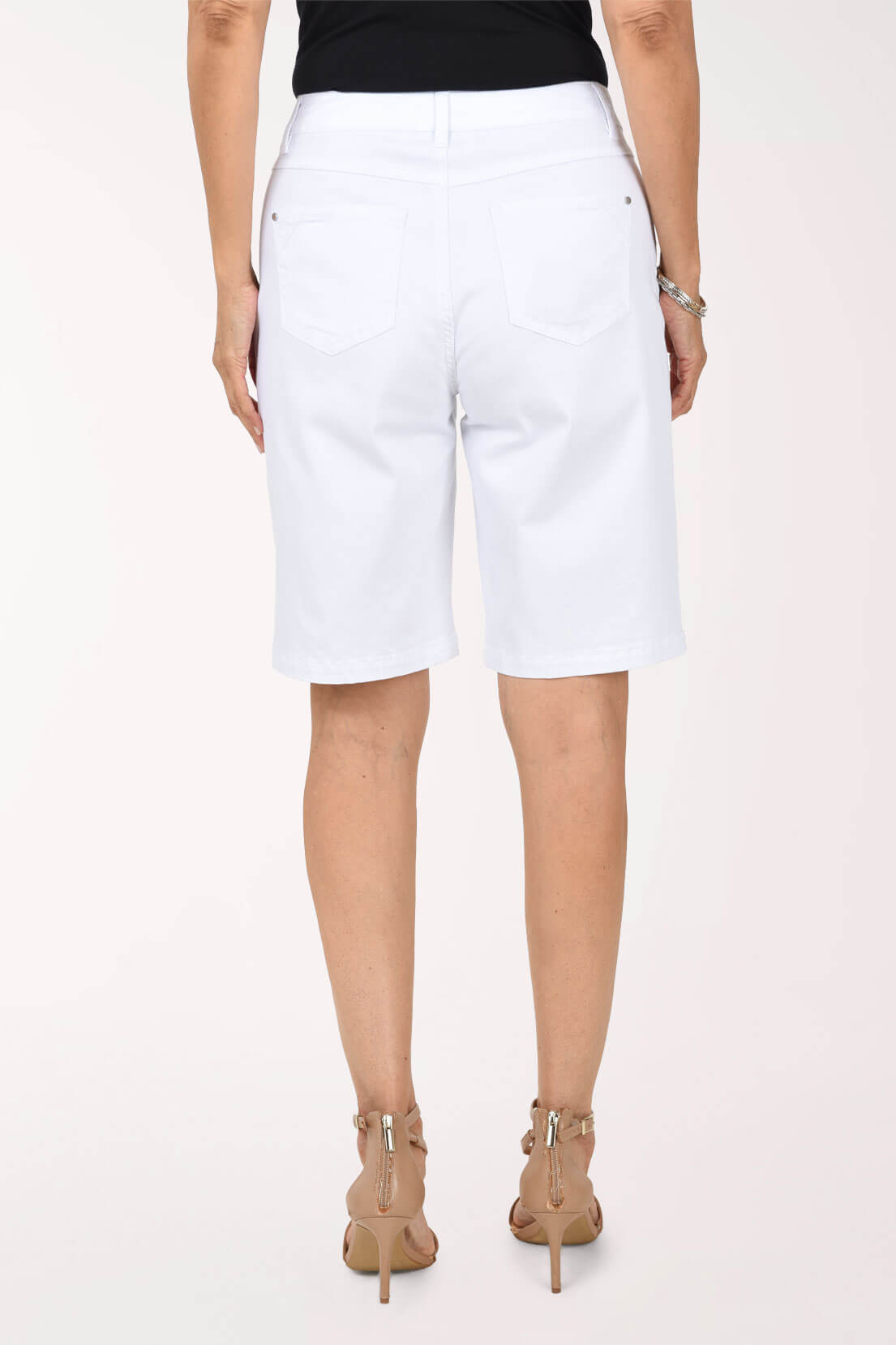 Back view of white stretch denim Bermuda shorts showing the back patch pockets, belt loops and straight hem, worn with nude heeled sandals.