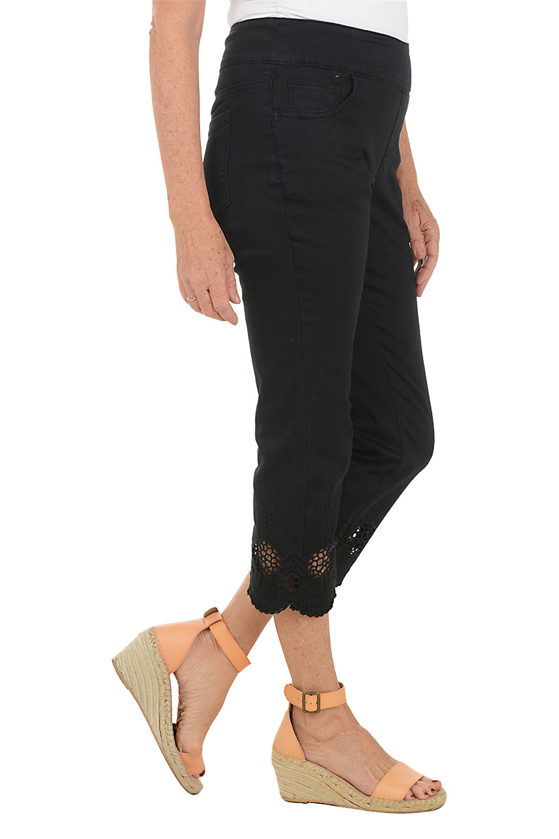 Black pants with floral embroidery at the bottom worn by a person on a white background. Side shot.