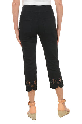 Black pants with floral embroidery at the bottom worn by a person on a white background. Back shot.