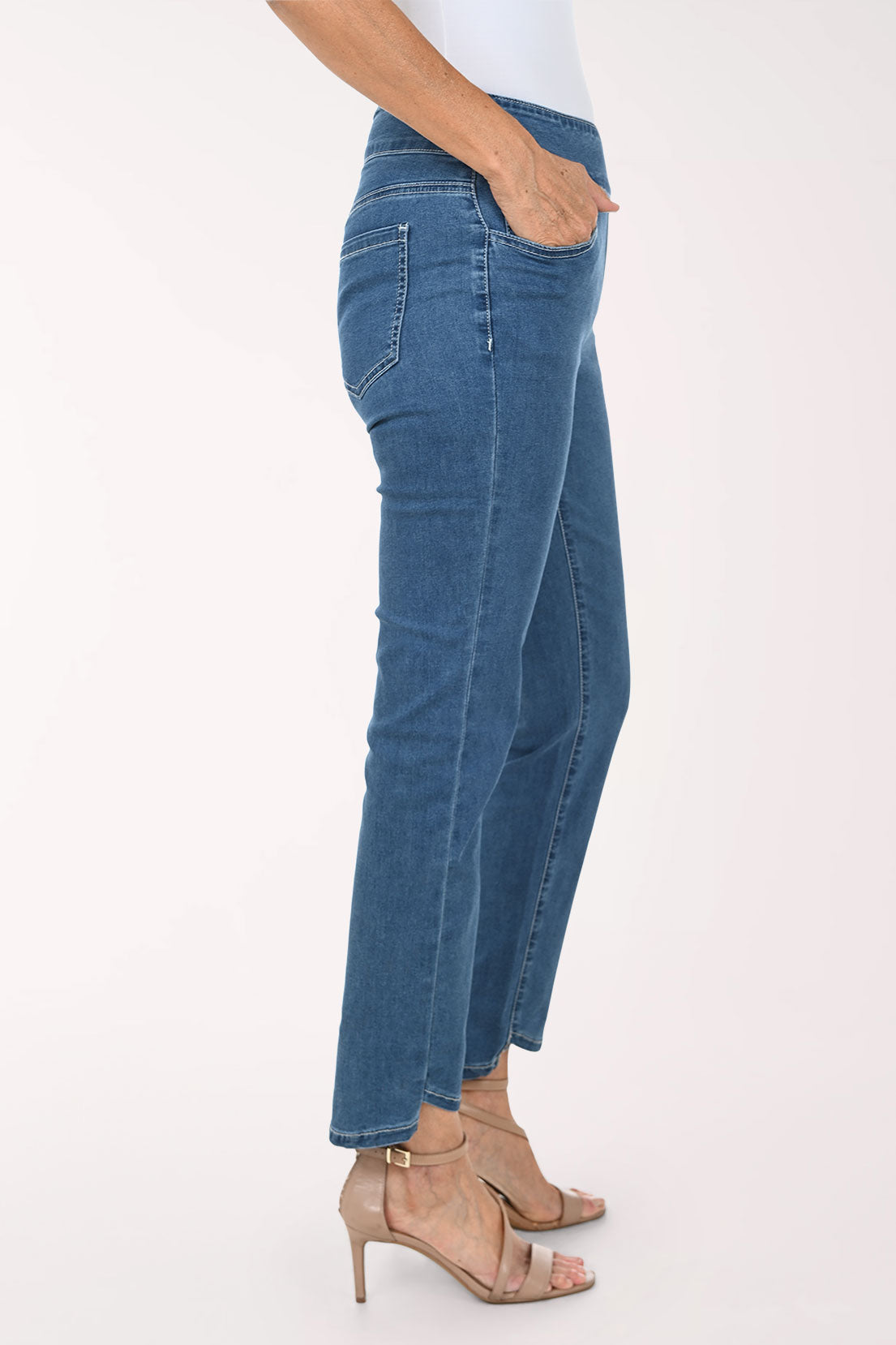 A model wearing medium wash blue denim jeans with a straight-to-regular leg fit, styled with beige high-heeled sandals against a plain white studio background.