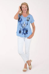 Full-length view of a woman in the Ethyl Clothing White Denim Stepped Hem Ankle Pant styled with a blue graphic tee and tan slide sandals.