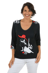 Woman wearing a black top with a graphic design of a woman in a red hat and white dress.
