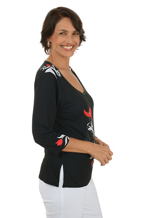 Woman wearing a black top with a graphic design of a woman in a red hat and white dress. Side shot.