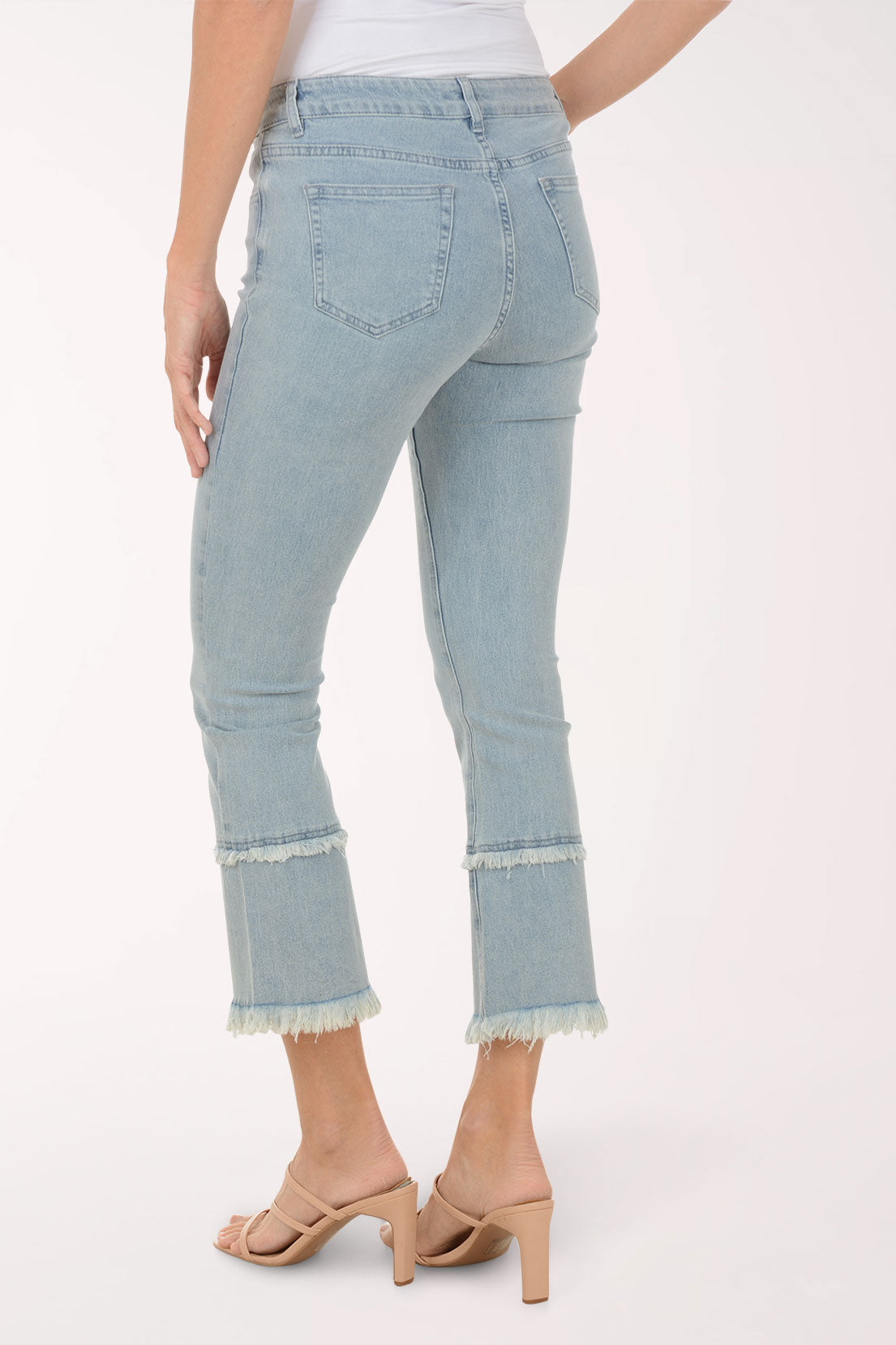 Light blue jeans with frayed hems worn by a person on a white background