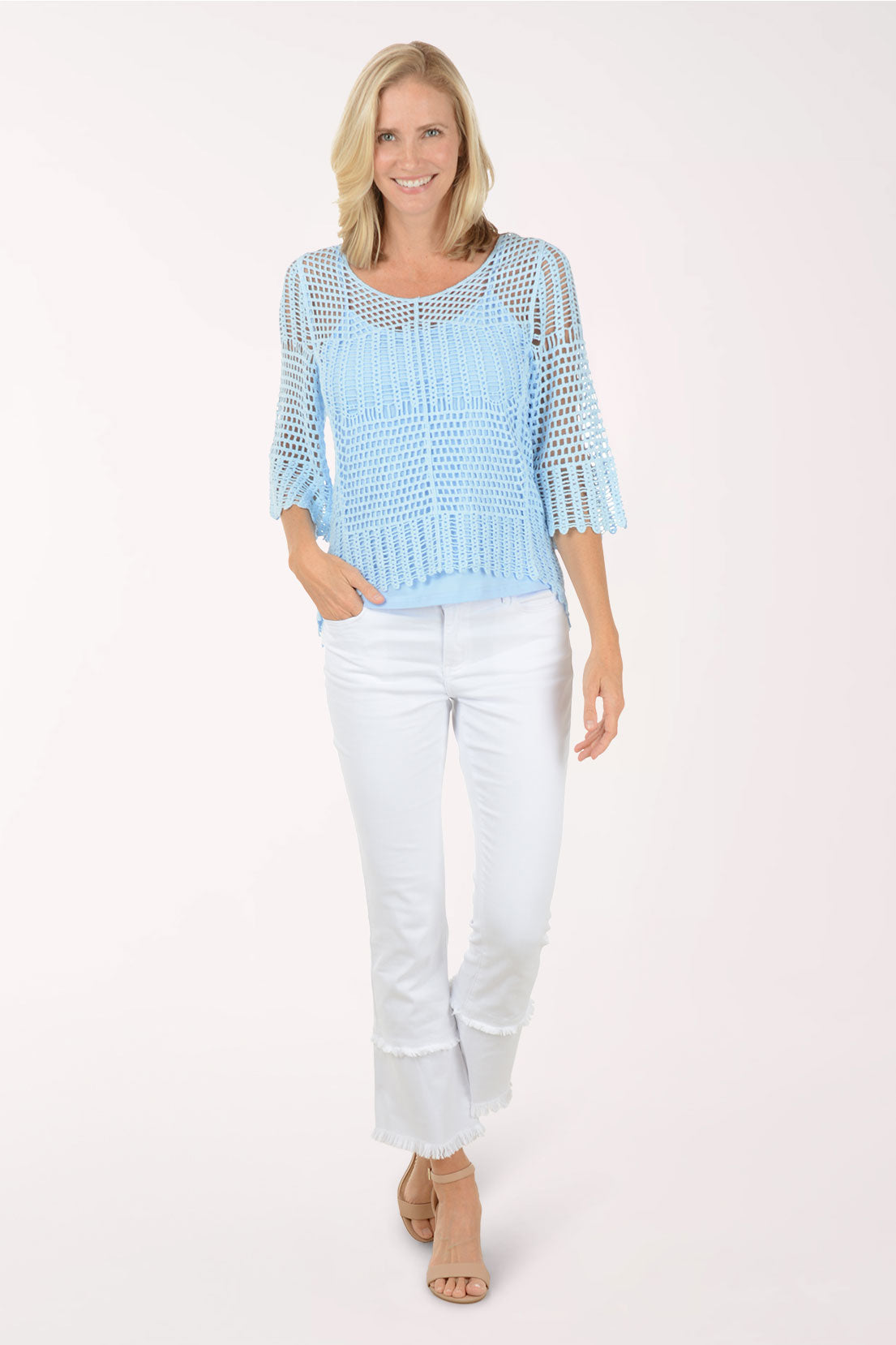 Woman wearing a light blue knit top with sheer sleeves and white pants on a white background