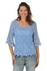 Woman wearing a blue crochet top and jeans on a white background.