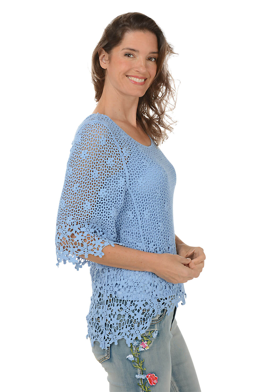 Woman wearing a blue crochet top and jeans on a white background. Side shot.