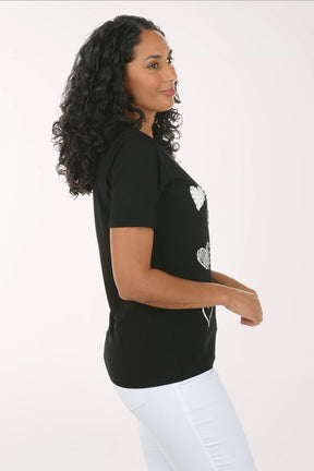 Woman wearing a black t-shirt with white heart patterns on a plain background