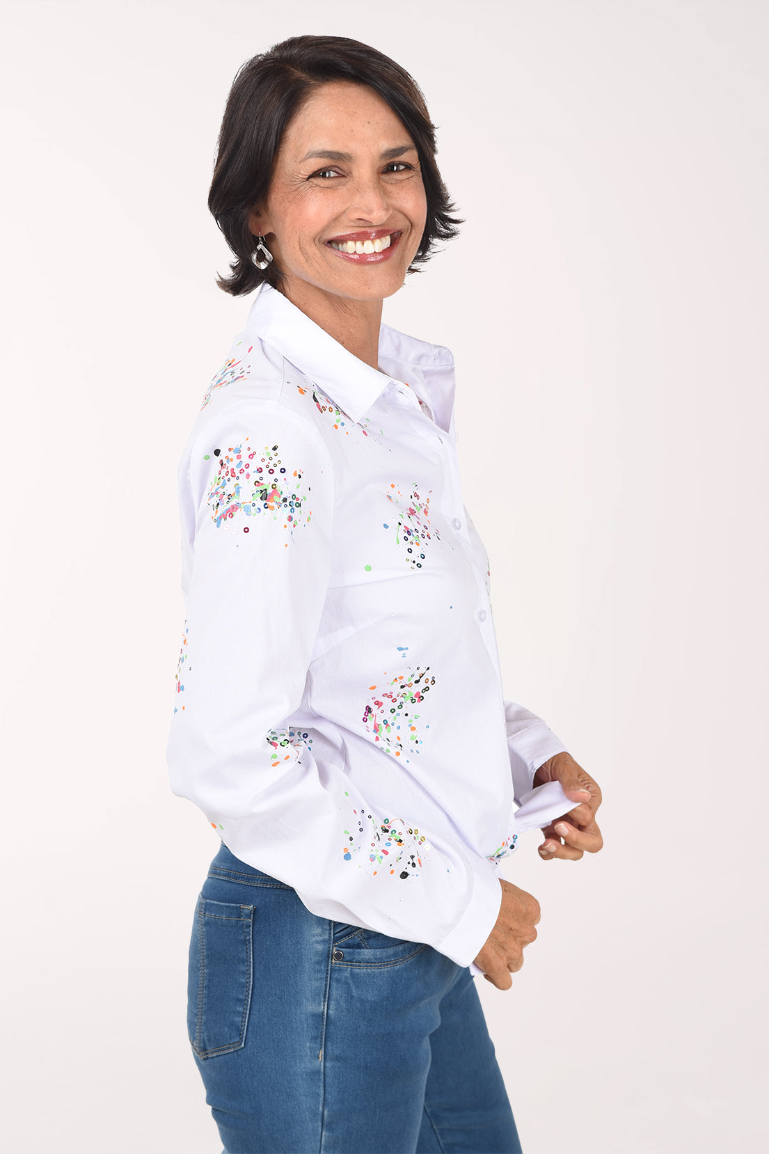Three-quarter view of the white speckled paint shirt showing the speckle clusters on the sleeve and front, worn with jeans.