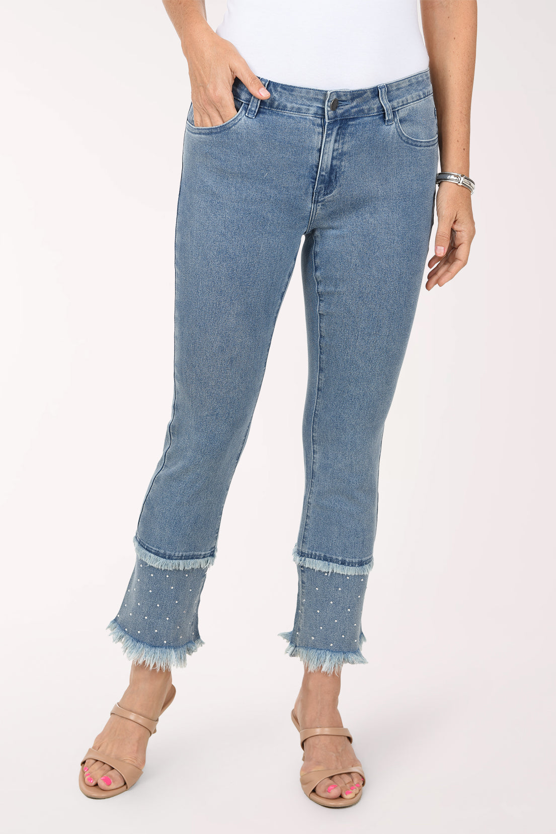 Front view of the light-wash fringe flared pants with one hand in the pocket, showing the five-pocket styling and the rhinestone-studded fringe tiers at the hem.