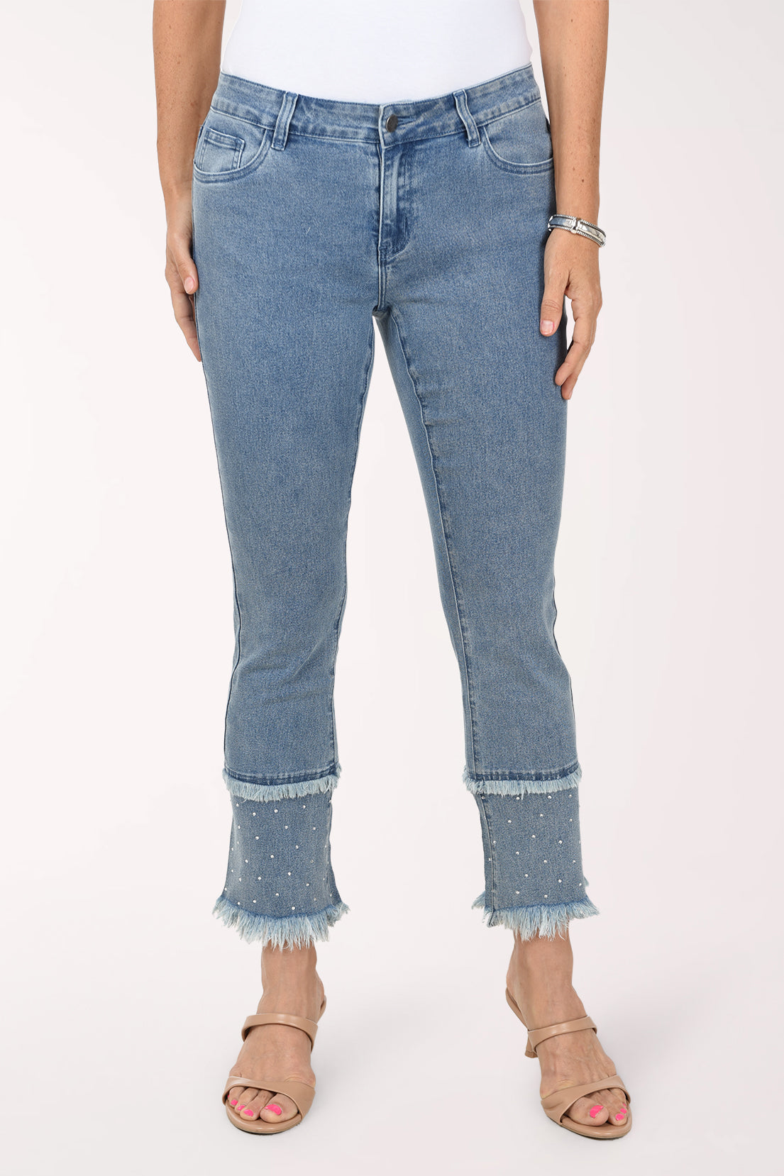 Front view of light-wash stretch denim ankle-length flared pants with a double fringed hem, the lower tier dotted with silver rhinestones, worn with a white top and nude heeled sandals.