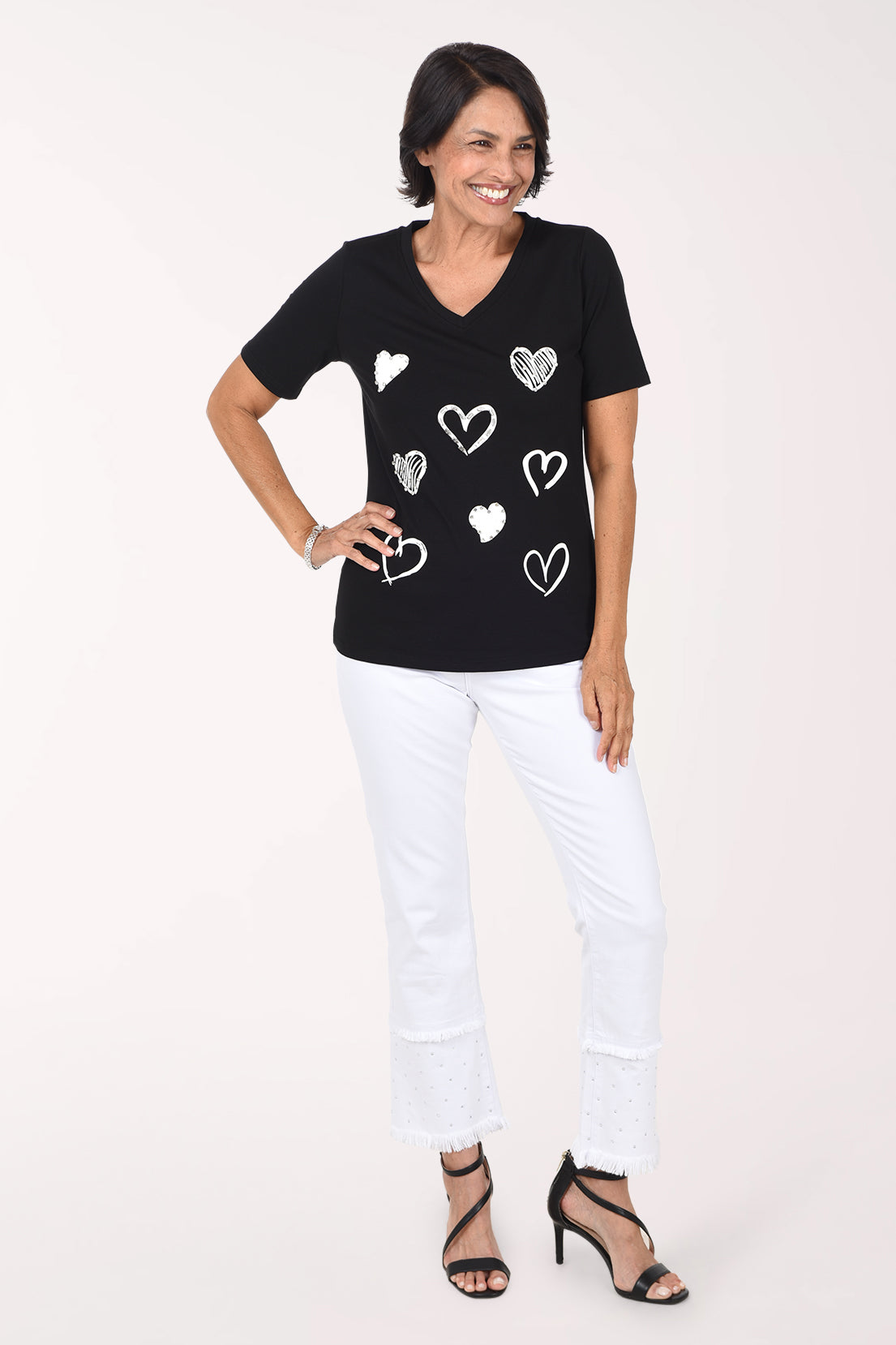 Front view of the white fringe flared pants with one hand on the hip, showing the ankle-length flare and layered fringe hem.