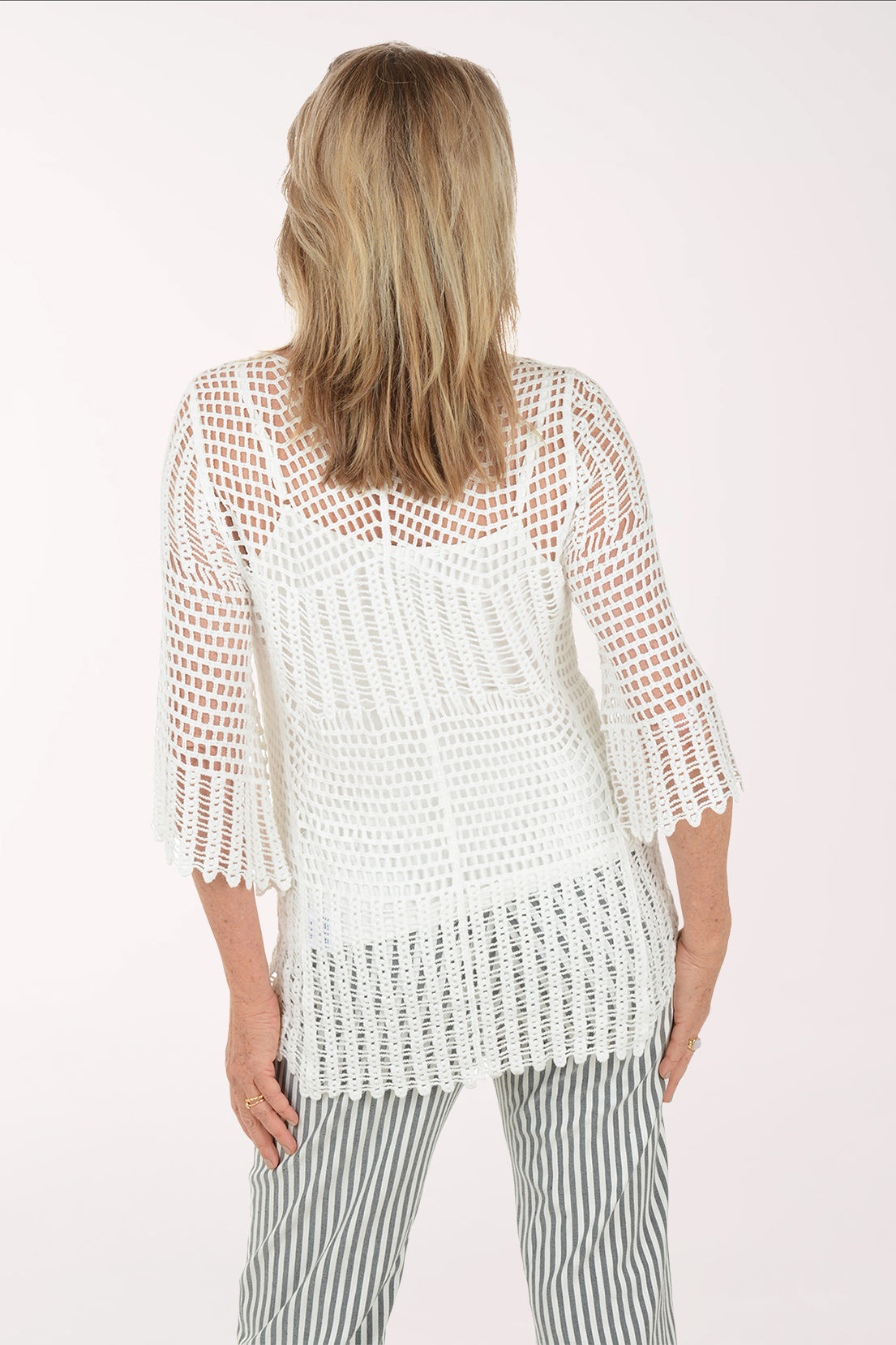 Woman wearing a white crochet top and striped pants on a white background