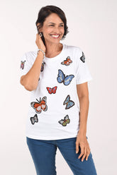 Front view of a woman in a white crew neck tee with rhinestone-outlined butterfly appliques in orange, blue, red and green, worn with medium-wash jeans.
