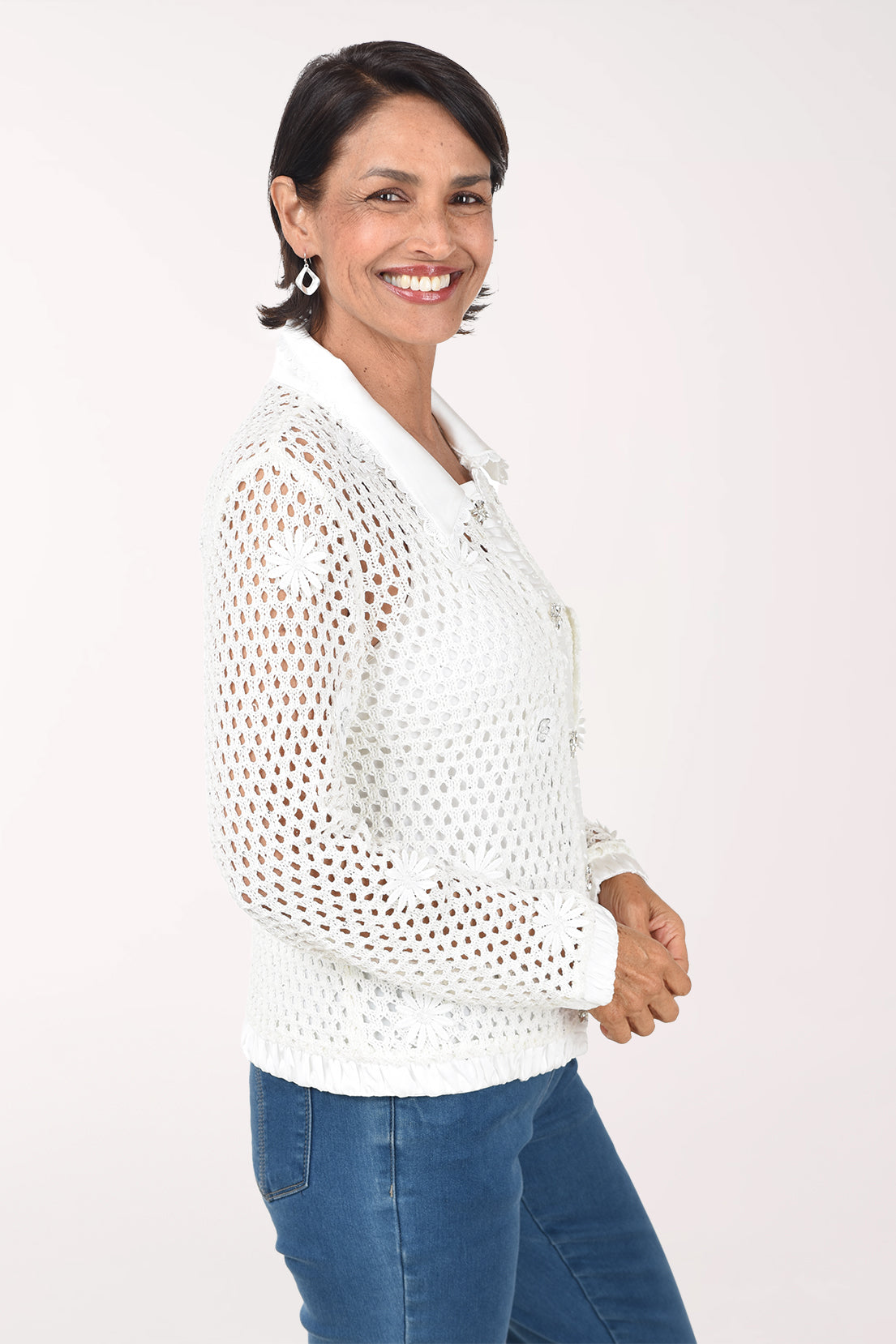 Three-quarter view of the ivory crochet sweater jacket showing the open crochet sleeve and satin cuff, worn with jeans.