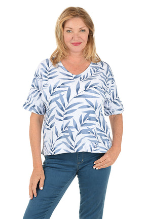Woman wearing a blue and white leaf-patterned top with blue jeans on a white background.