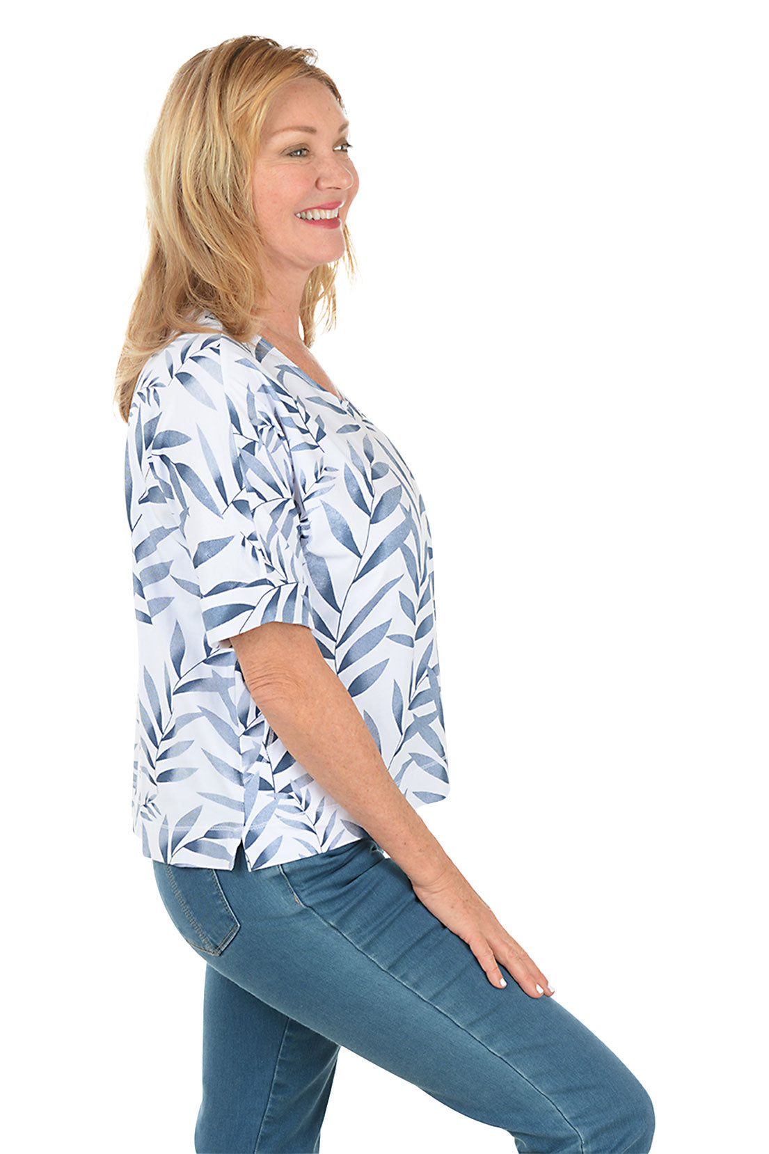 Woman wearing a blue and white leaf-patterned top with blue jeans on a white background. Side shot.