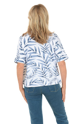 Woman wearing a blue and white leaf-patterned top with blue jeans on a white background. Back shot.