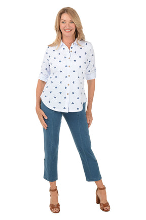 Woman wearing a white blouse with blue heart patterns and blue jeans on a white background.