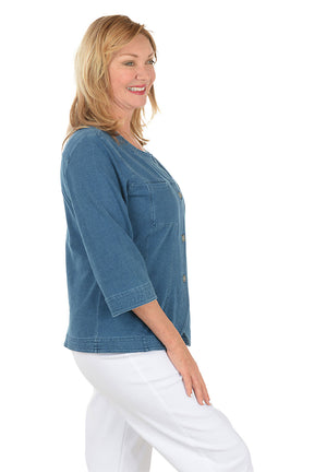 Woman wearing a blue denim shirt with a white background. Side shot.