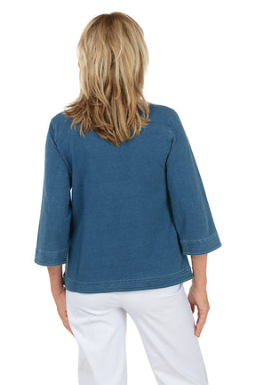 Woman wearing a blue denim shirt with a white background. Back shot.