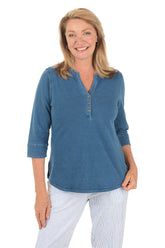 Woman wearing a blue long-sleeve shirt and white pants on a white background.