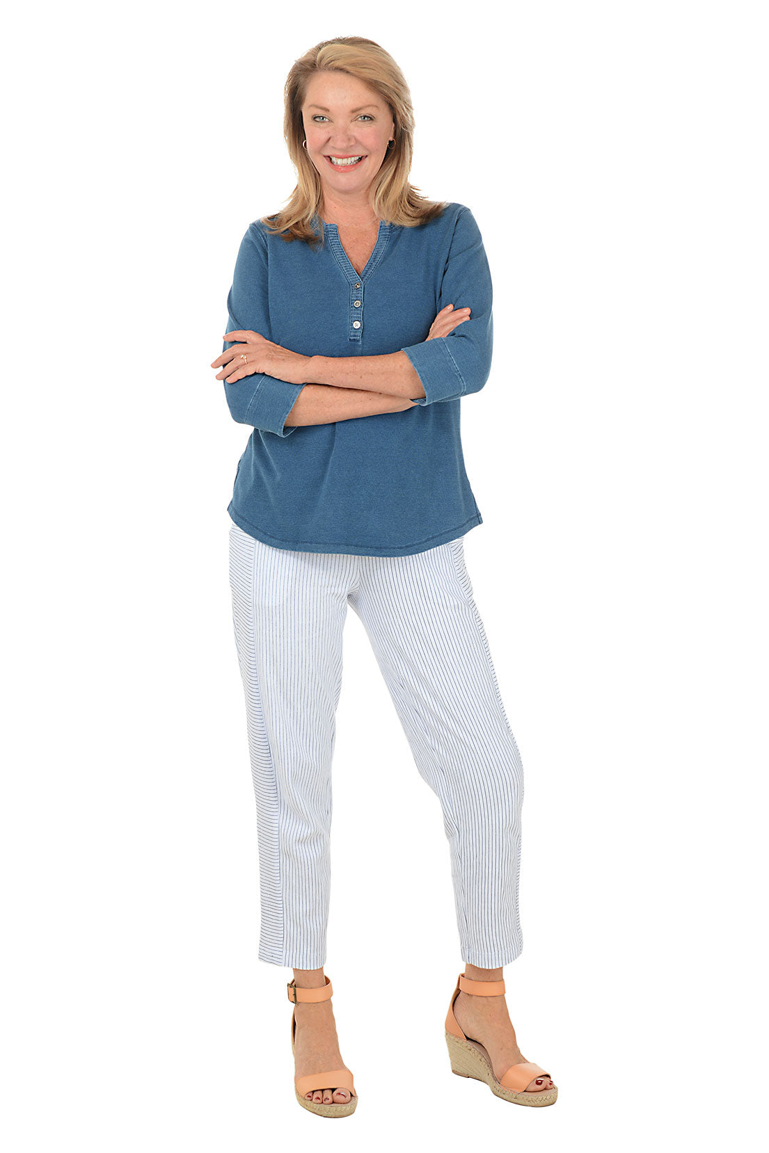 Woman wearing a blue shirt and white pants with a white background. Second full length shot.