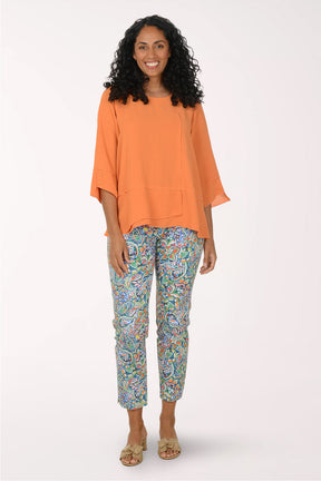 Woman wearing an orange top and colorful patterned pants on a white background