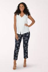 Woman wearing a white sleeveless top and navy pants with a pattern on a white background