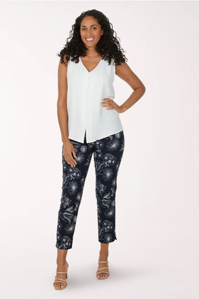 Woman wearing a white sleeveless top and navy pants with a pattern on a white background