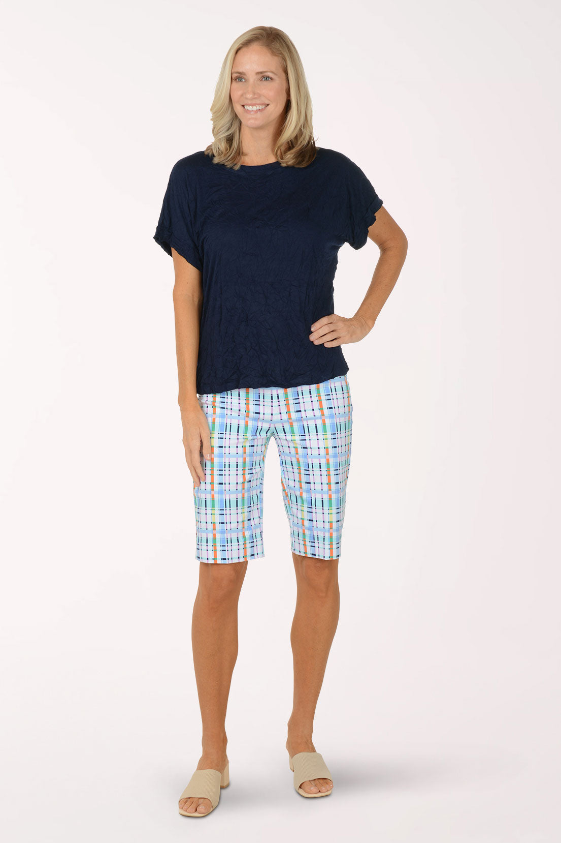 Woman wearing a navy blue top and colorful plaid shorts on a white background