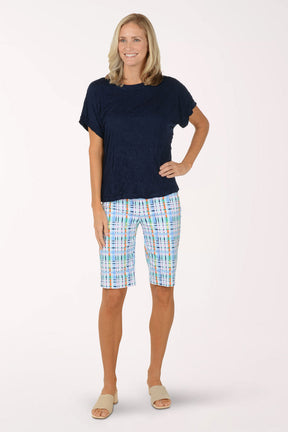 Woman wearing a navy blue top and colorful plaid shorts on a white background