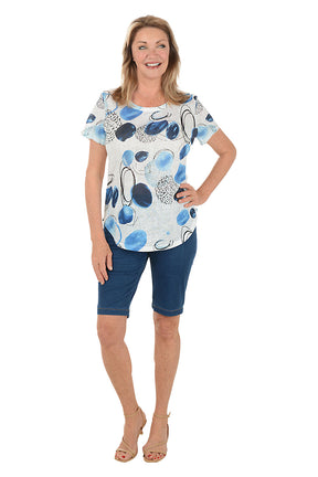 Woman wearing a patterned top and blue shorts on a white background